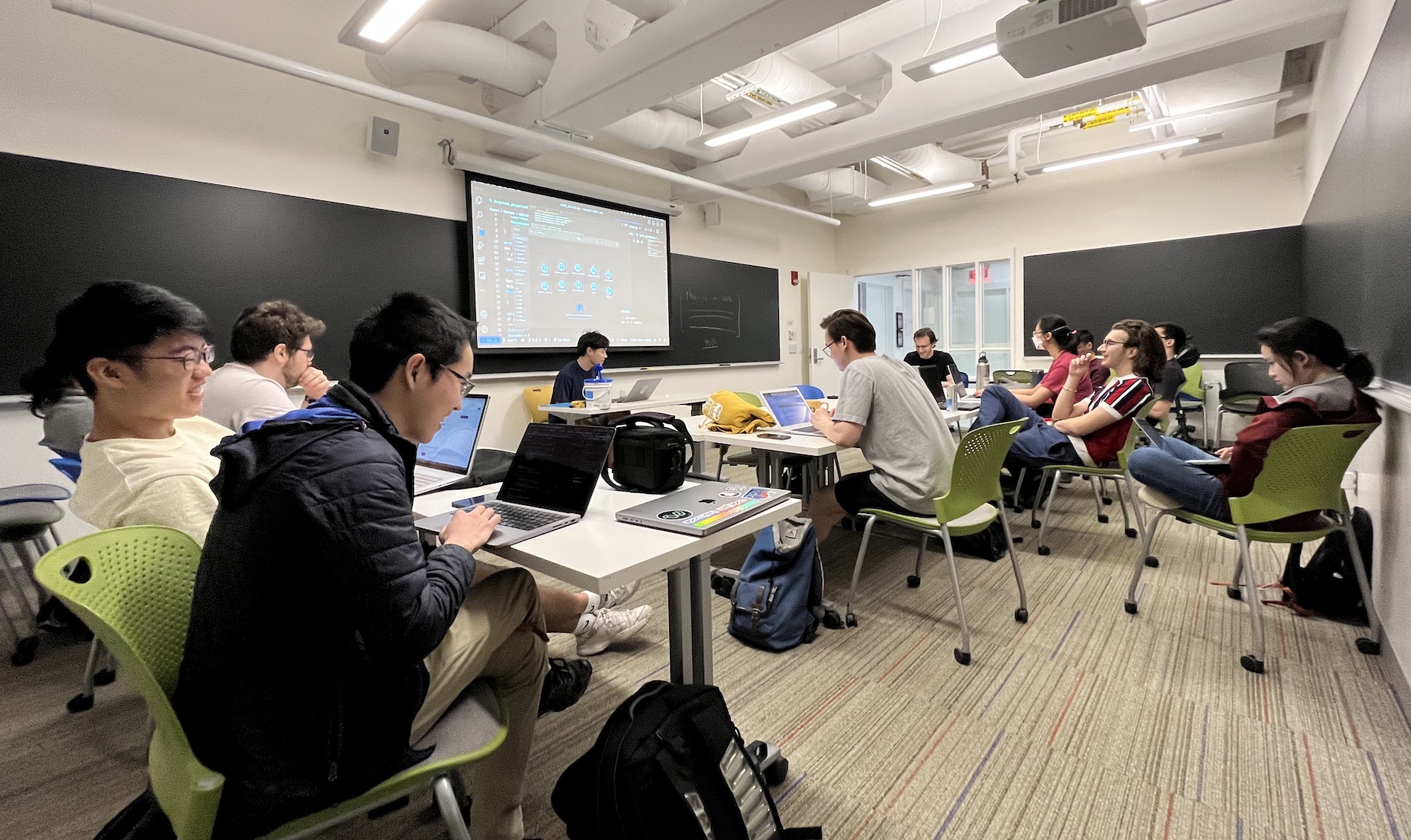 A group of people sitting around a table, smiling and looking at a projector